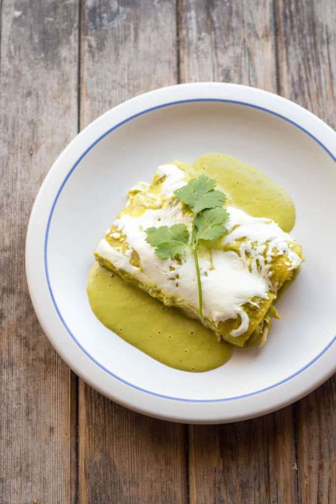 Top view of two enchiladas suiza on a white plate garnished with cilantro.