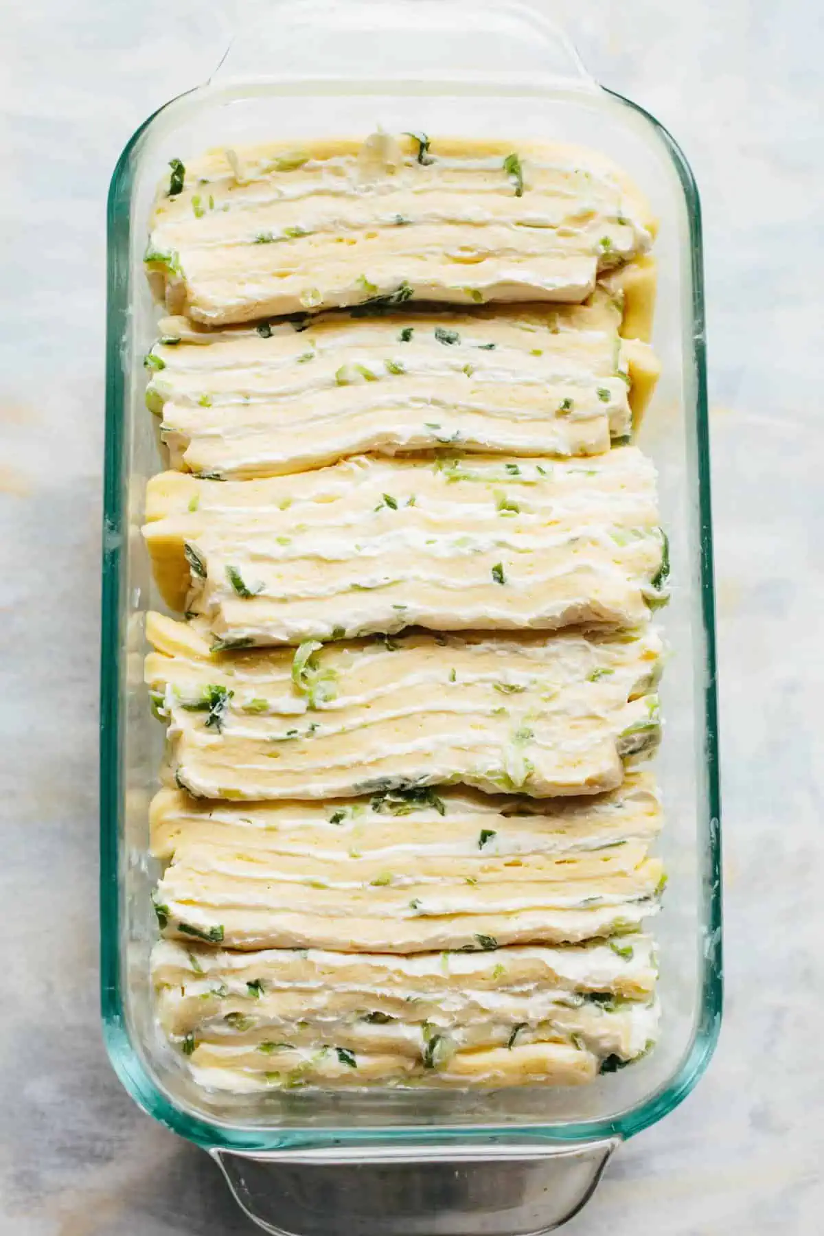 Pre-baked pull apart bread dough and cream cheese layered vertically in a glass loaf pan.