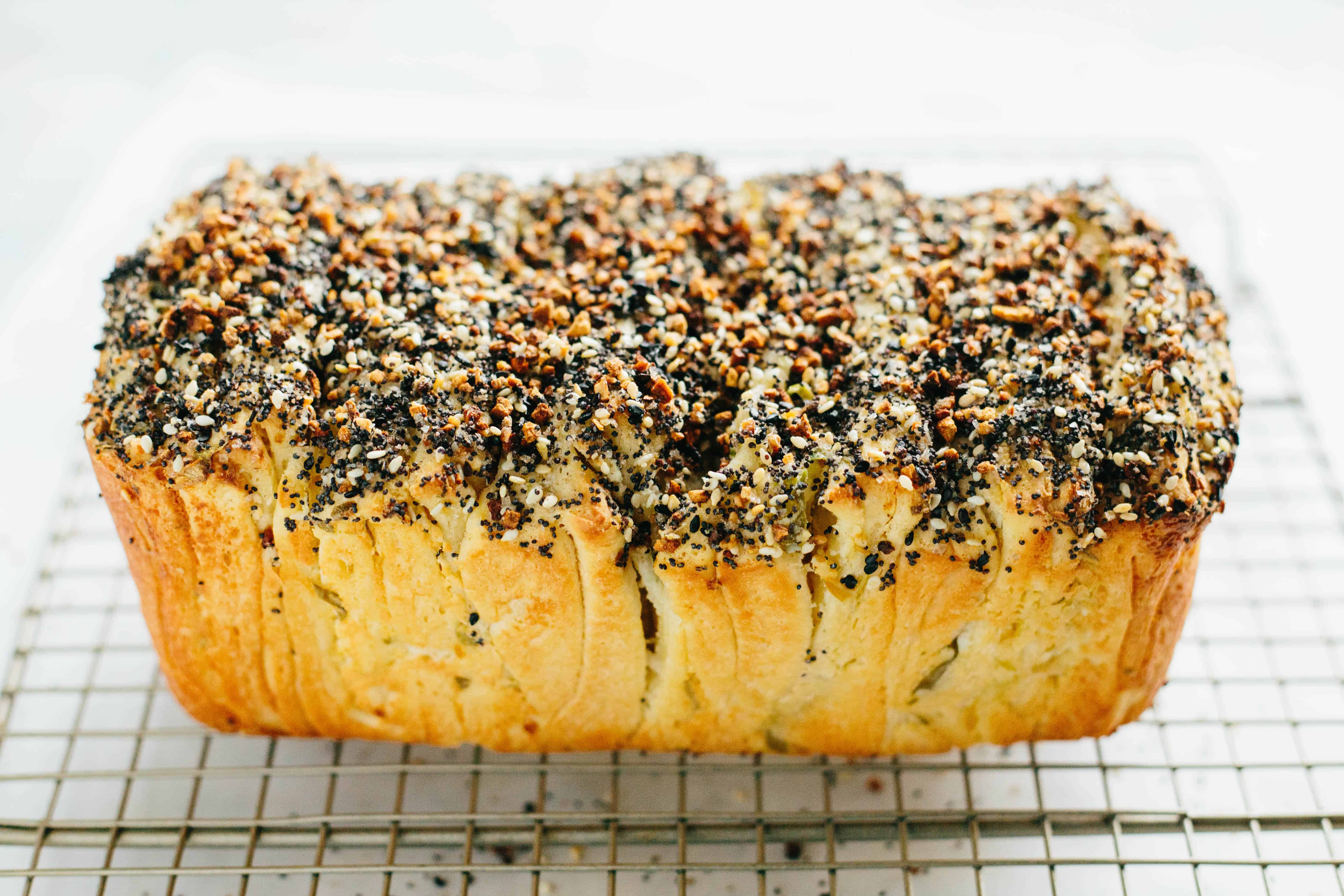 Side view of a loaf of everything bagel pull apart bread sitting on a wire cooling rack.