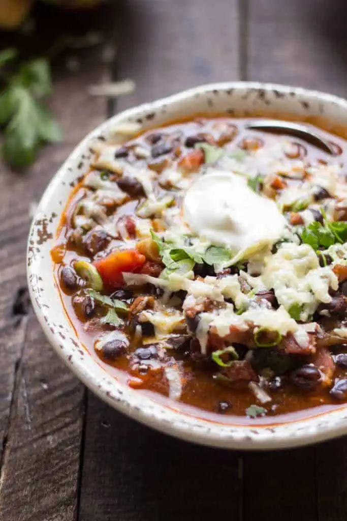 Close up of black bean soup with bacon in a bowl and topped with sour cream.