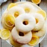 Meyer lemon baked doughnuts piled high on a plate with thinly sliced lemon.