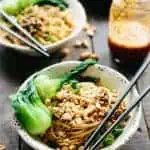 A bowl of dan dan noodles and baby bok choy with chopsticks.