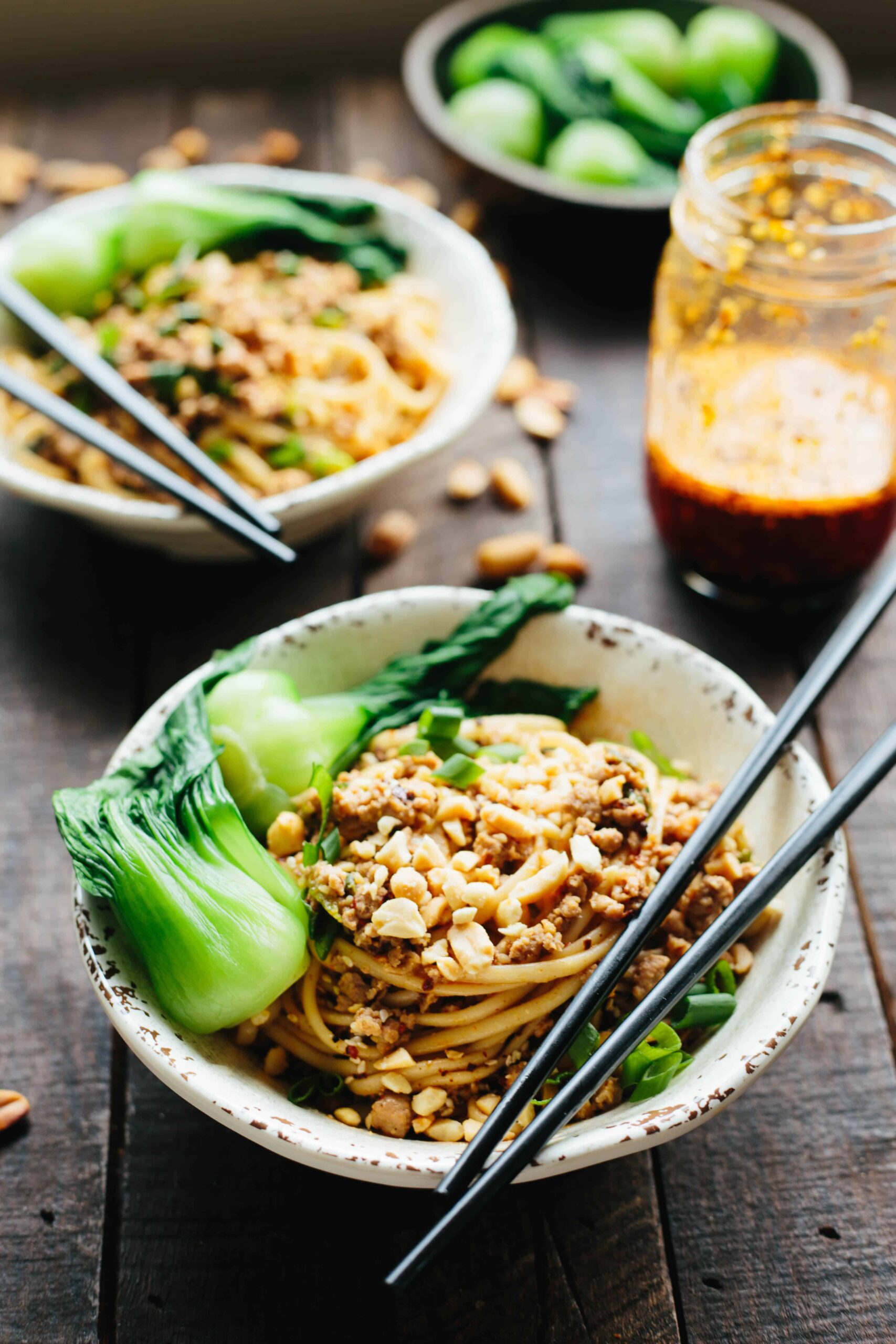 A bowl of dan dan noodles and baby bok choy with chopsticks.