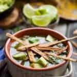 A brown bowl of chicken tortilla soup topped with diced avocado and fried tortilla strips.