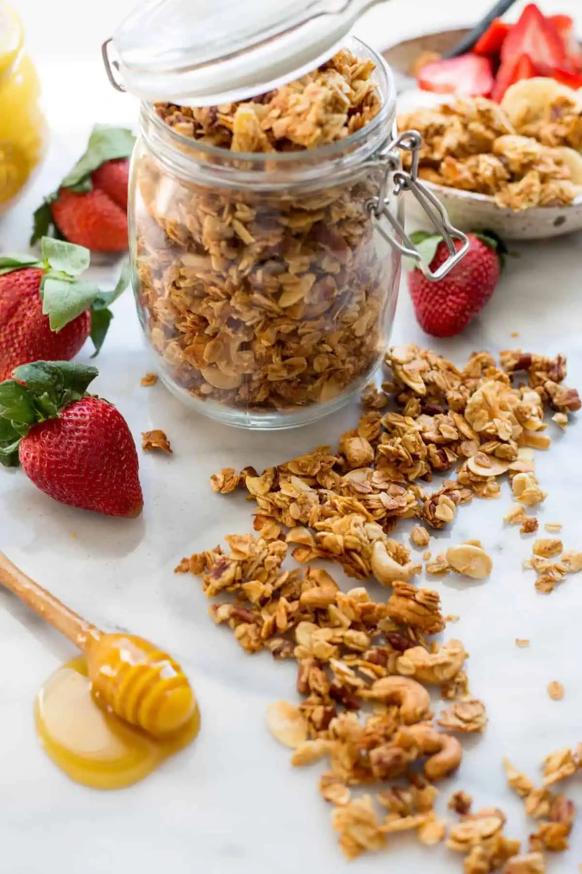 A glass jar of honey butter granola with some spilled out on the counter.