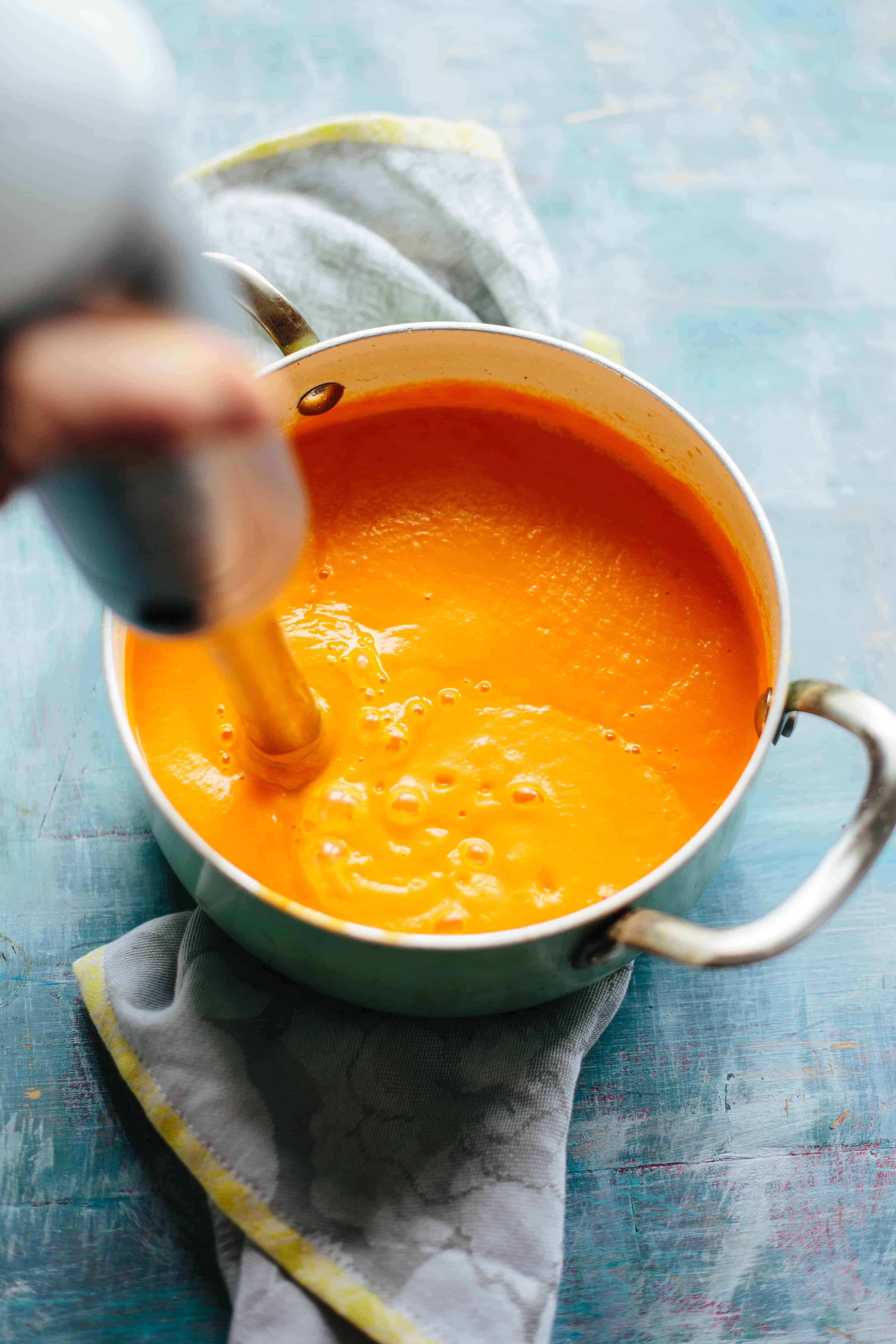 A stick blender pureeing carrot soup in a large pot.