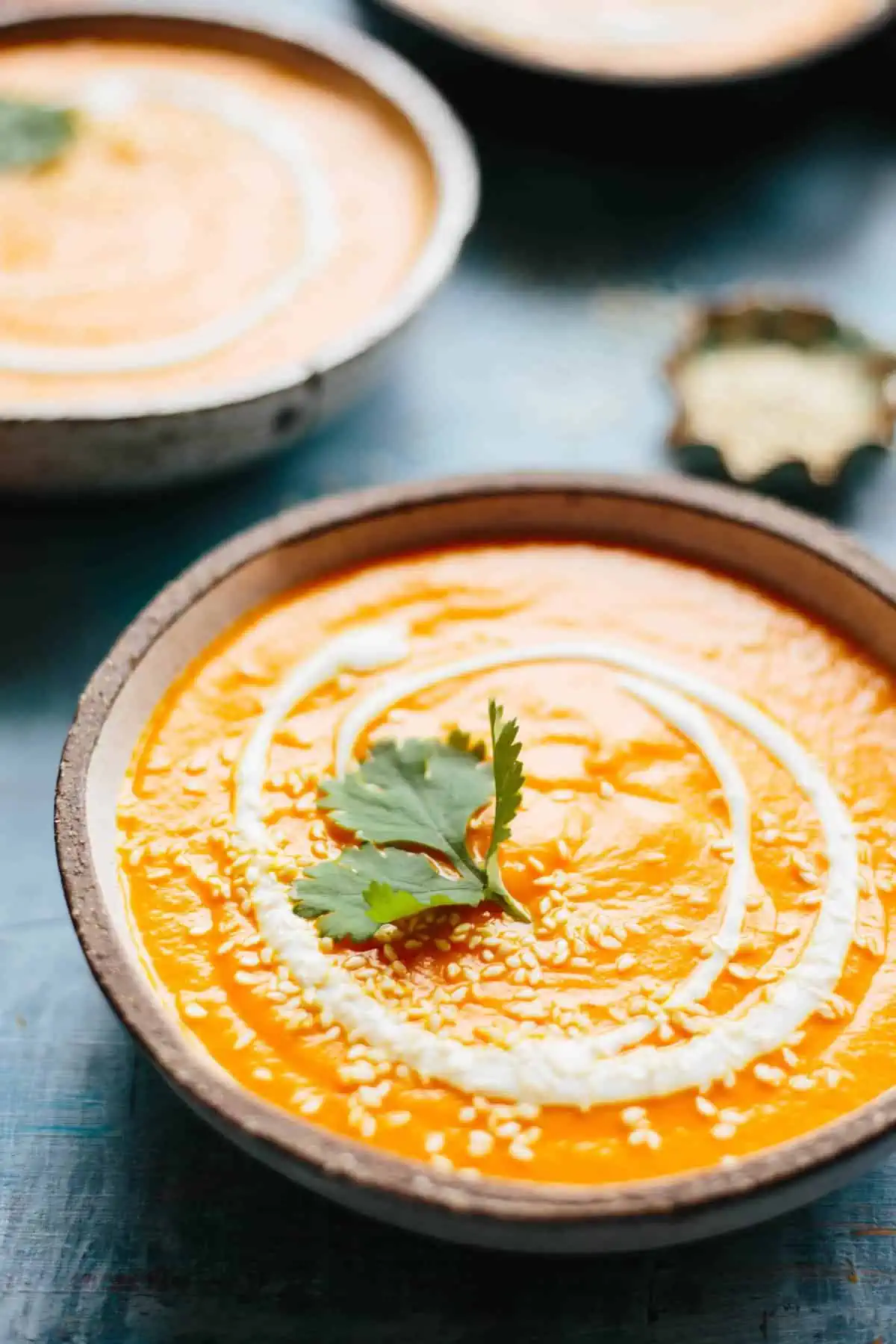 Close up of a bowl of pureed carrot soup garnished with yogurt swirl and sesame seeds.