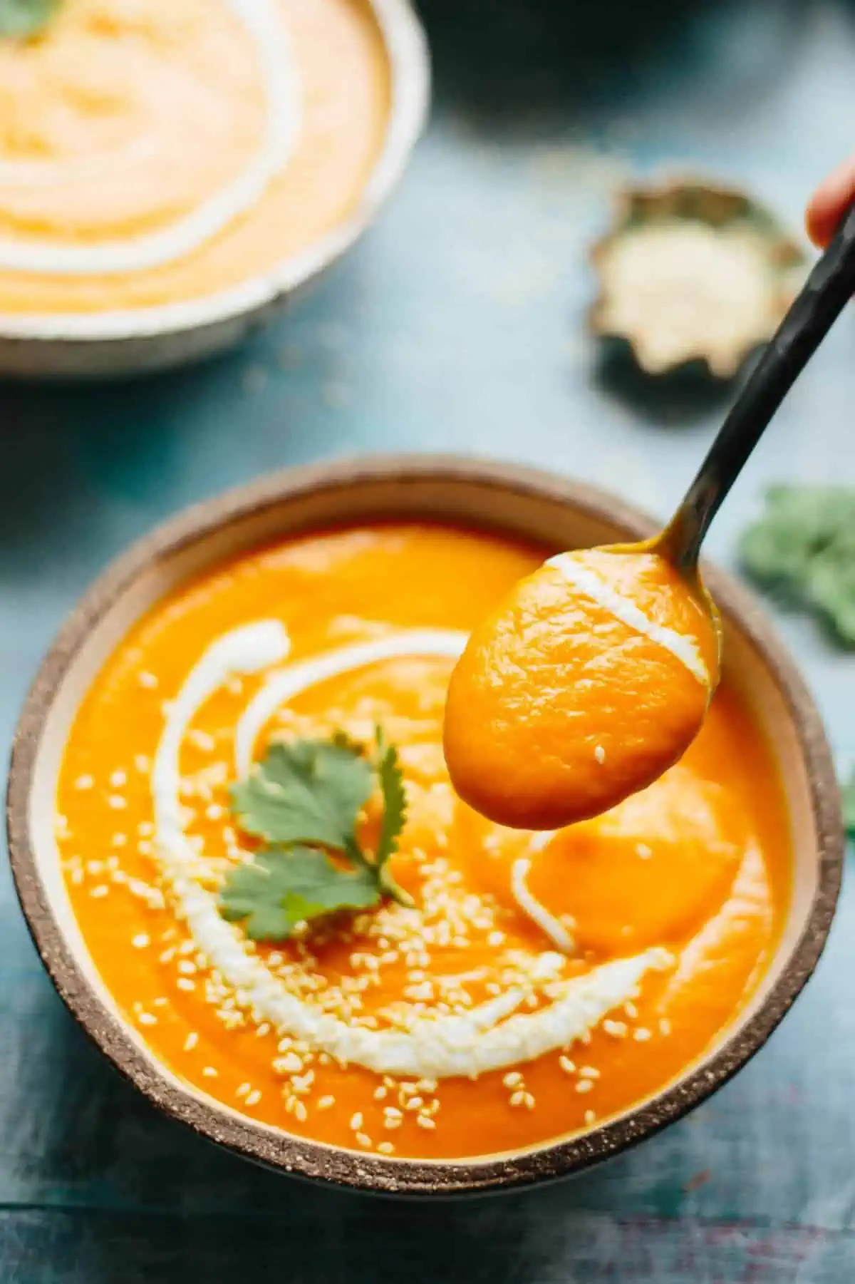 A spoon that has dipped into a bowl of spicy carrot soup.