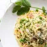 Top view of linguini carbonara with peas in a shallow white bowl.