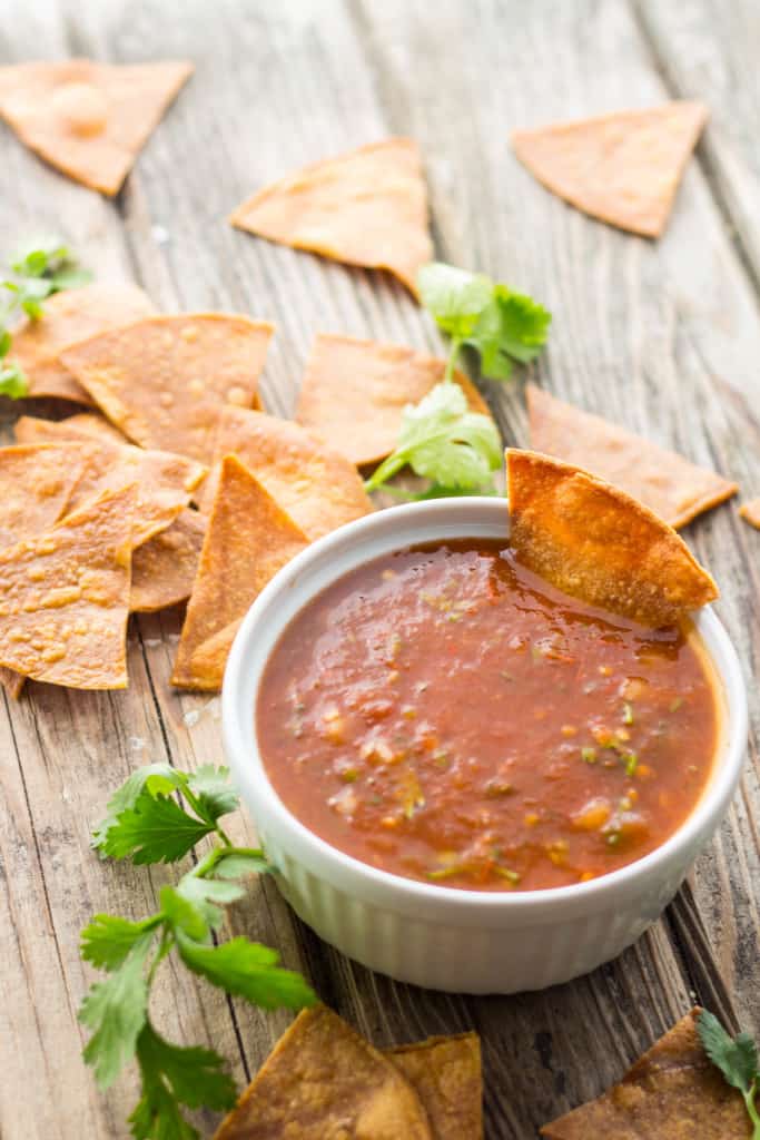 Fresh fried tortilla chips on a table next to a bowl of authentic Mexican tomato salsa.