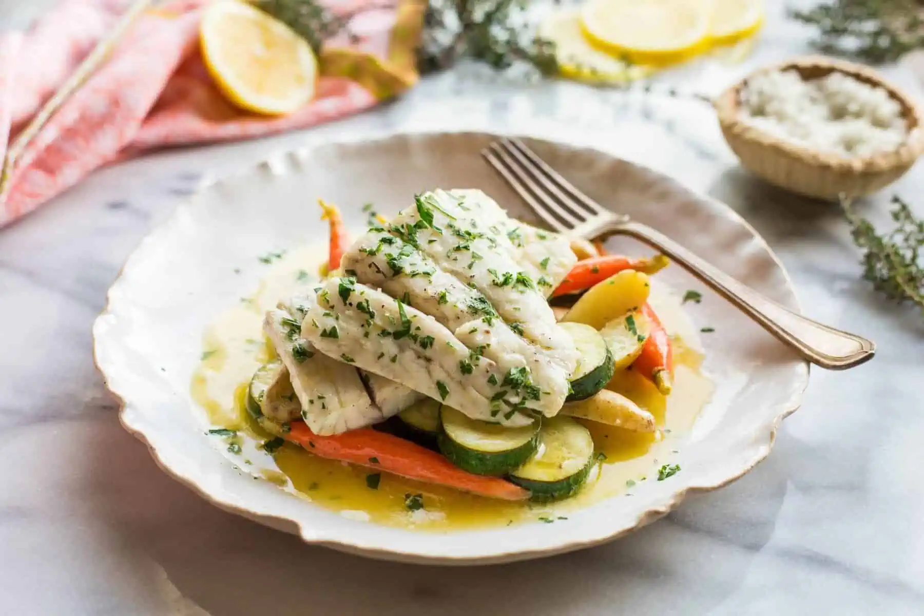 Butter poached fish fillets layered over vegetables in a shallow bowl.