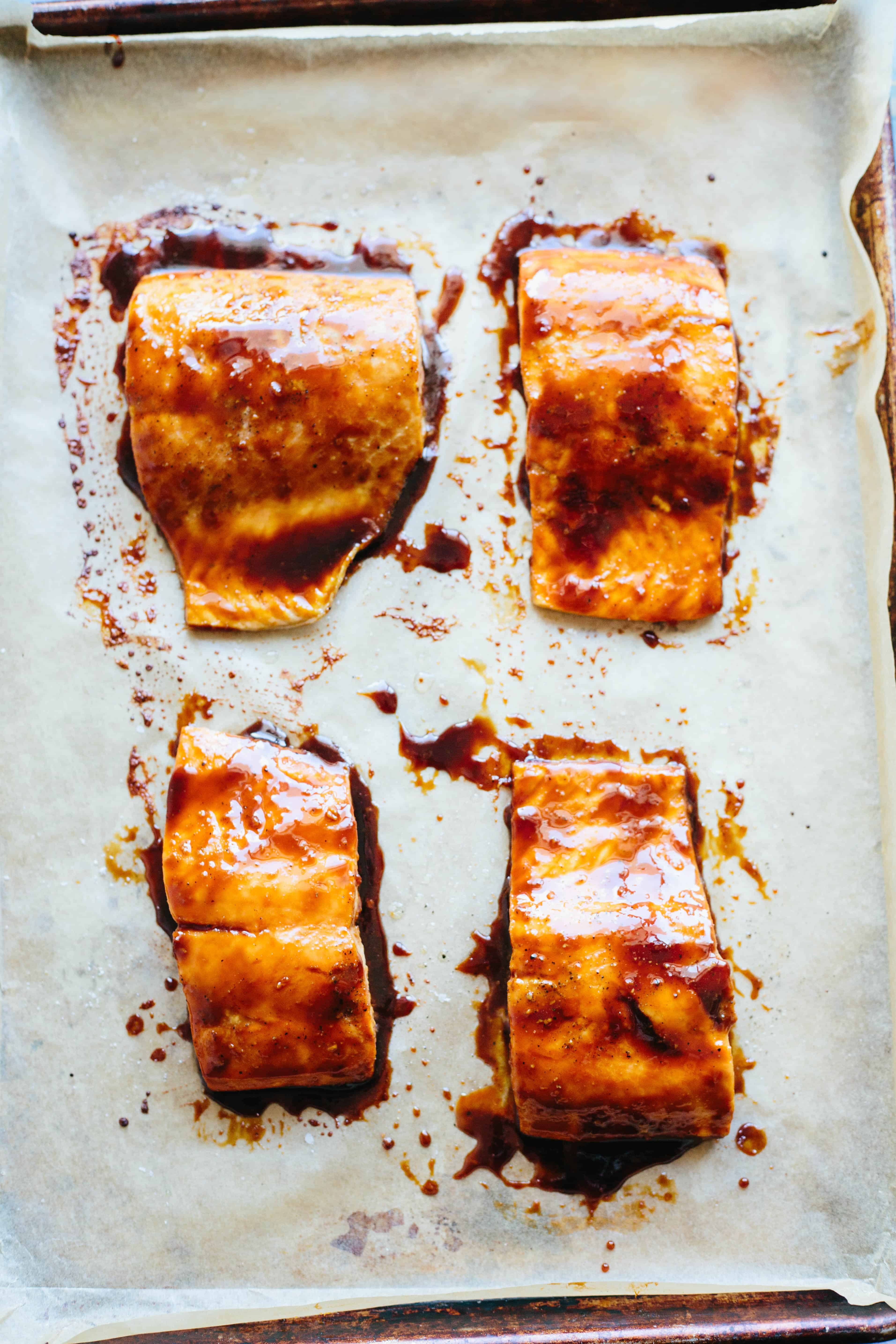 Four soy-glazed salmon filets on a parchment-lined baking sheet.