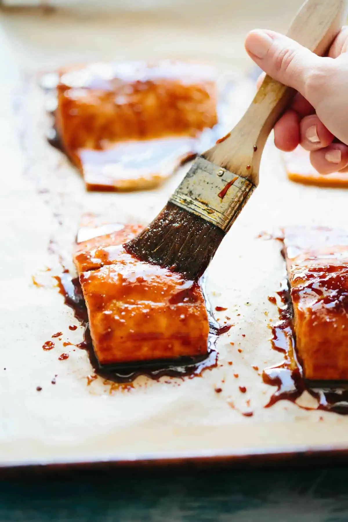 Using a pastry brush to add soy glaze to a salmon fillet.