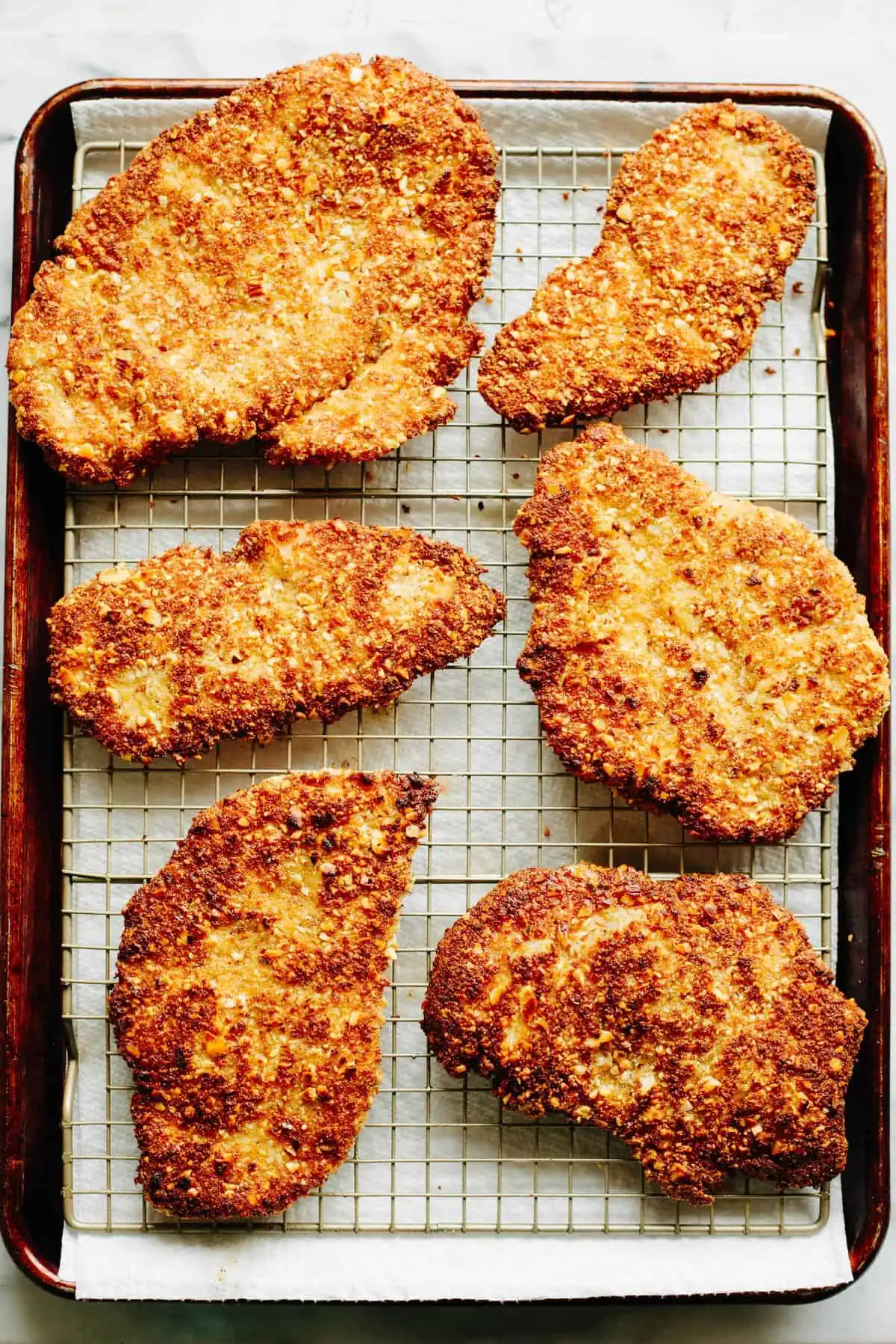 Almond breaded chicken cutlets draining on a wire rack over a baking sheet.