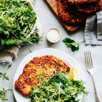 Vertical shot of an almond crusted chicken cutlet with arugula salad on a plate.