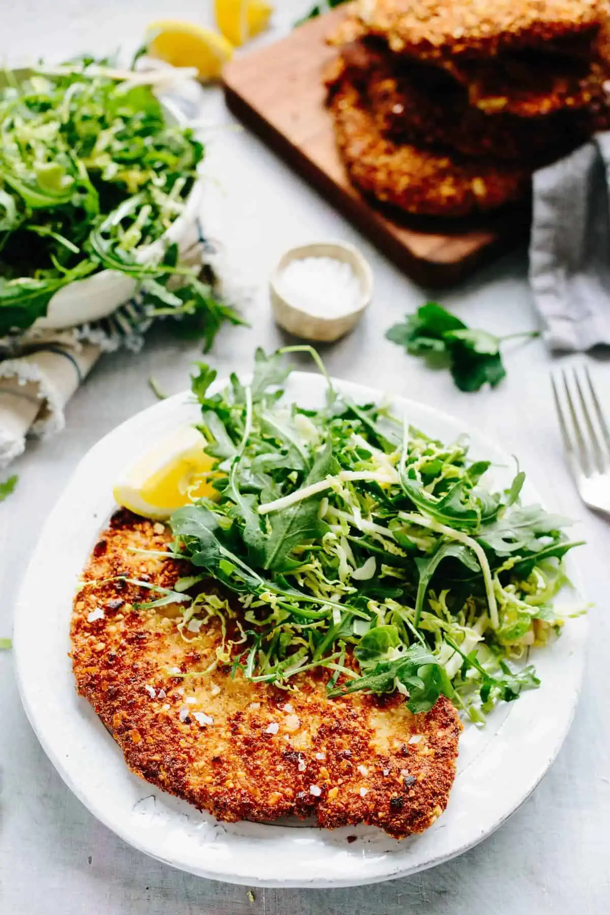 Vertical shot of a white dinner plate containing arugula salad and a breaded chicken cutlet.