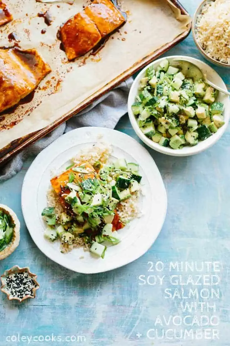 Top view of a dinner plate of rice, salmon fillet, and diced avocado, next to a bowl of avocado cucumber salad.