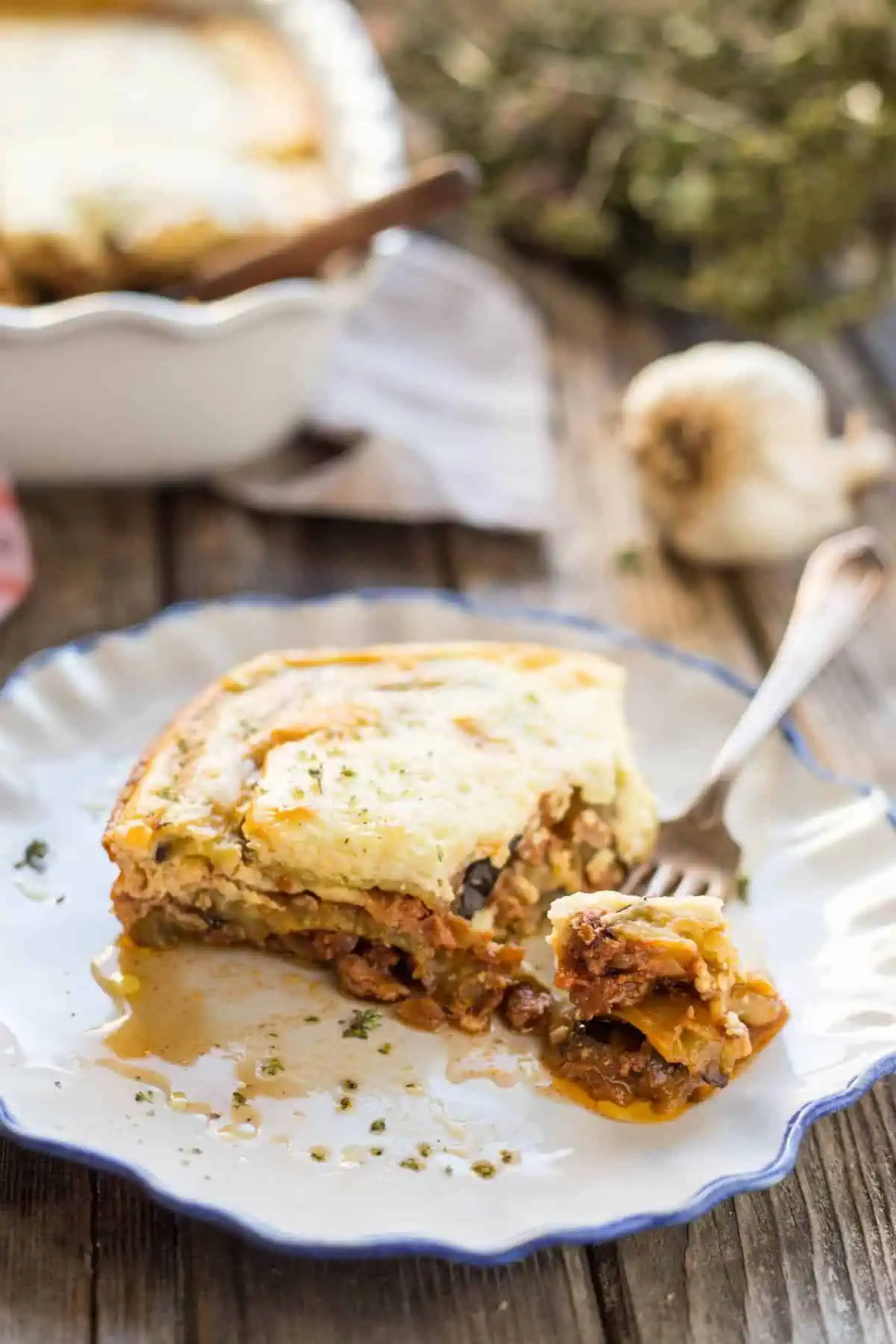 Corner slice of moussaka on a dinner plate with a fork holding a bite.