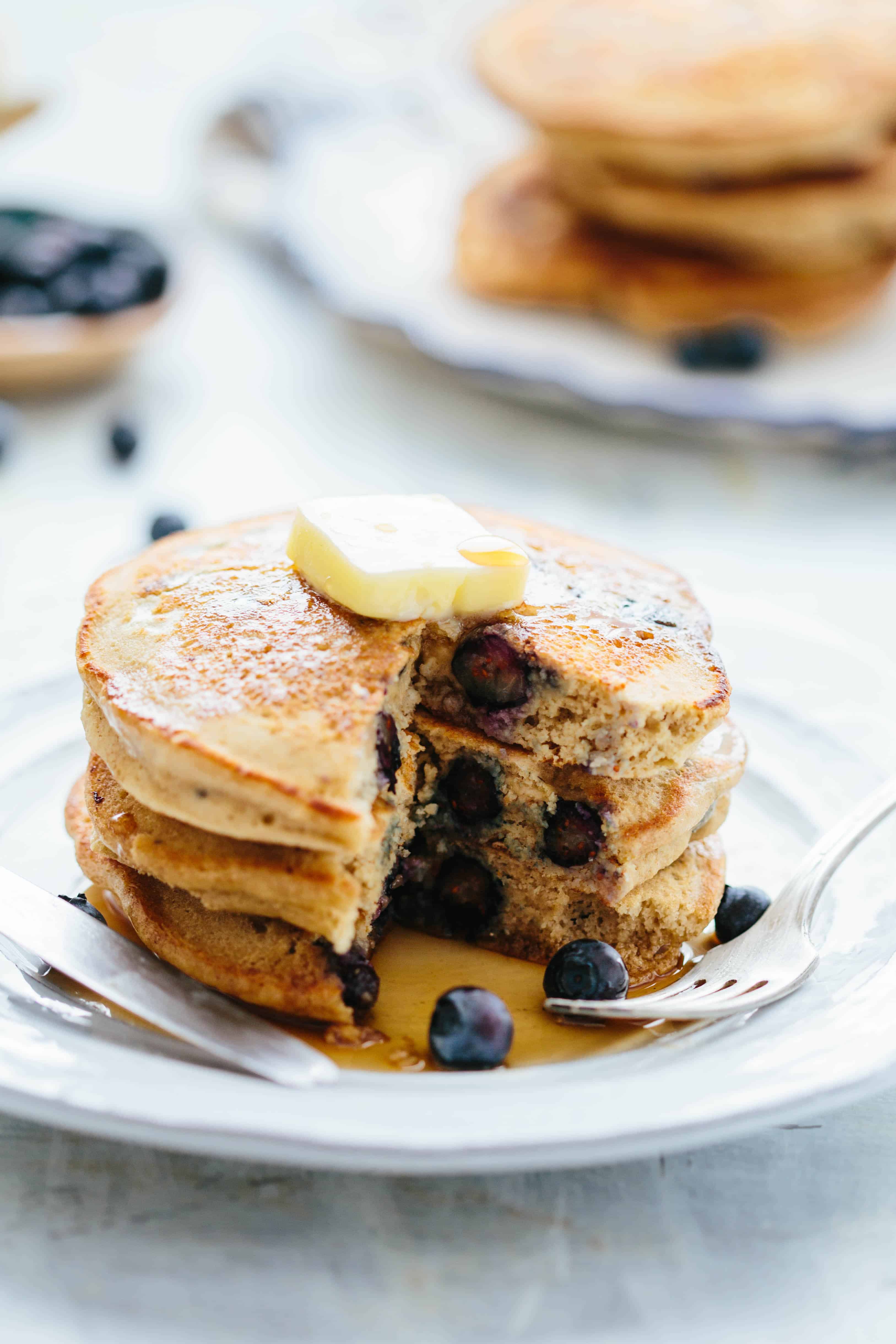 A close up of a stack of blueberry oatmeal pancakes that has a wedge sliced out of them.