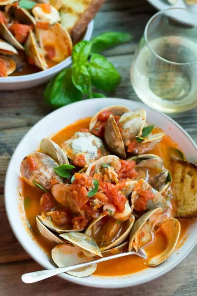 Baked clams in tomato sauce in a white serving bowl.
