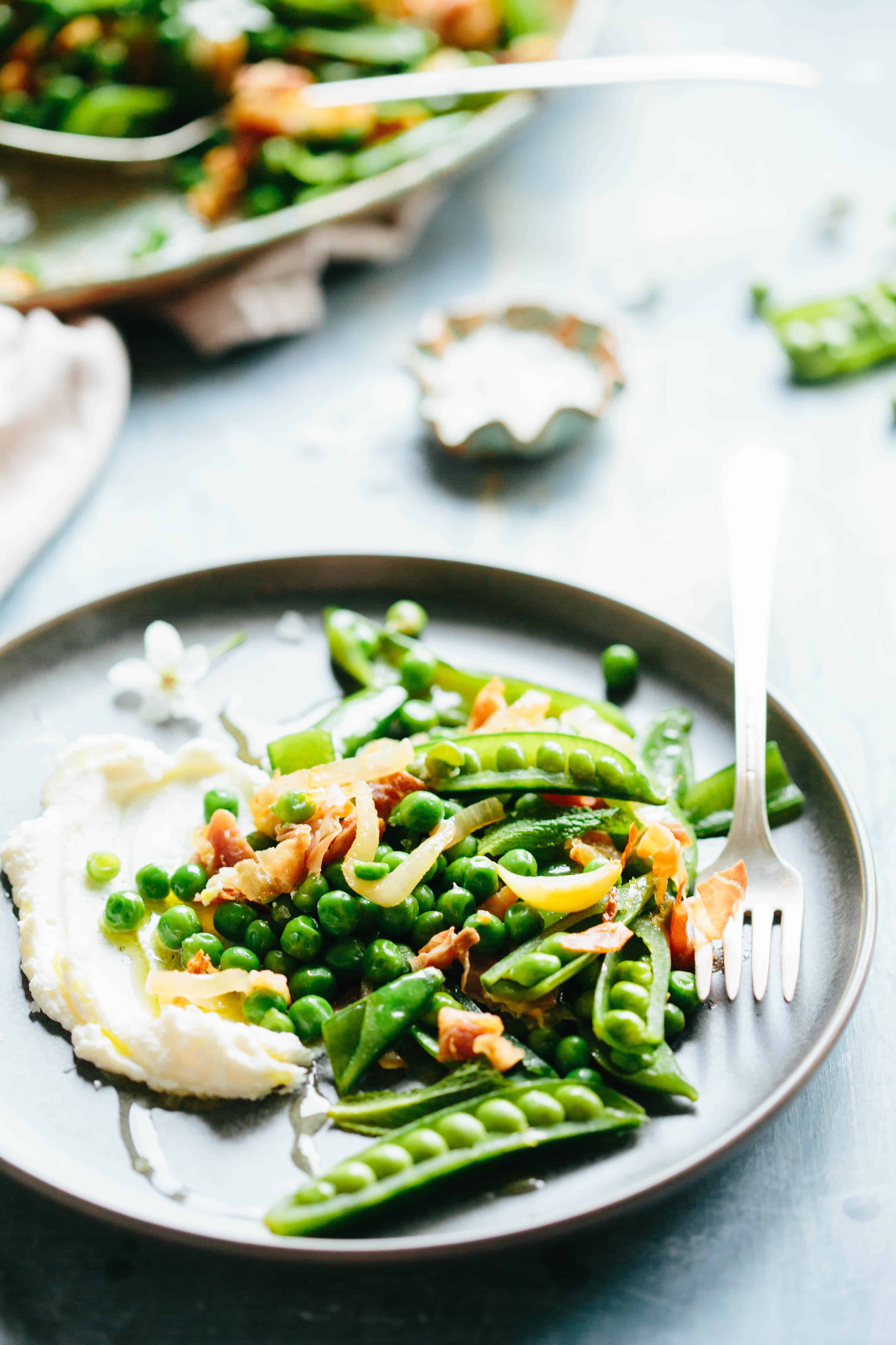 Plate with creamy ricotta that has crispy prosciutto and spring pea pods on top.