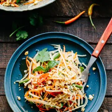Thai flavored papaya salad piled up on a blue plate with a fork.