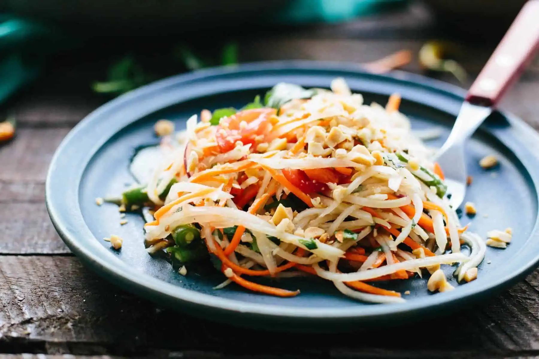 Side view of a plate piled with shredded Thai green papaya salad.