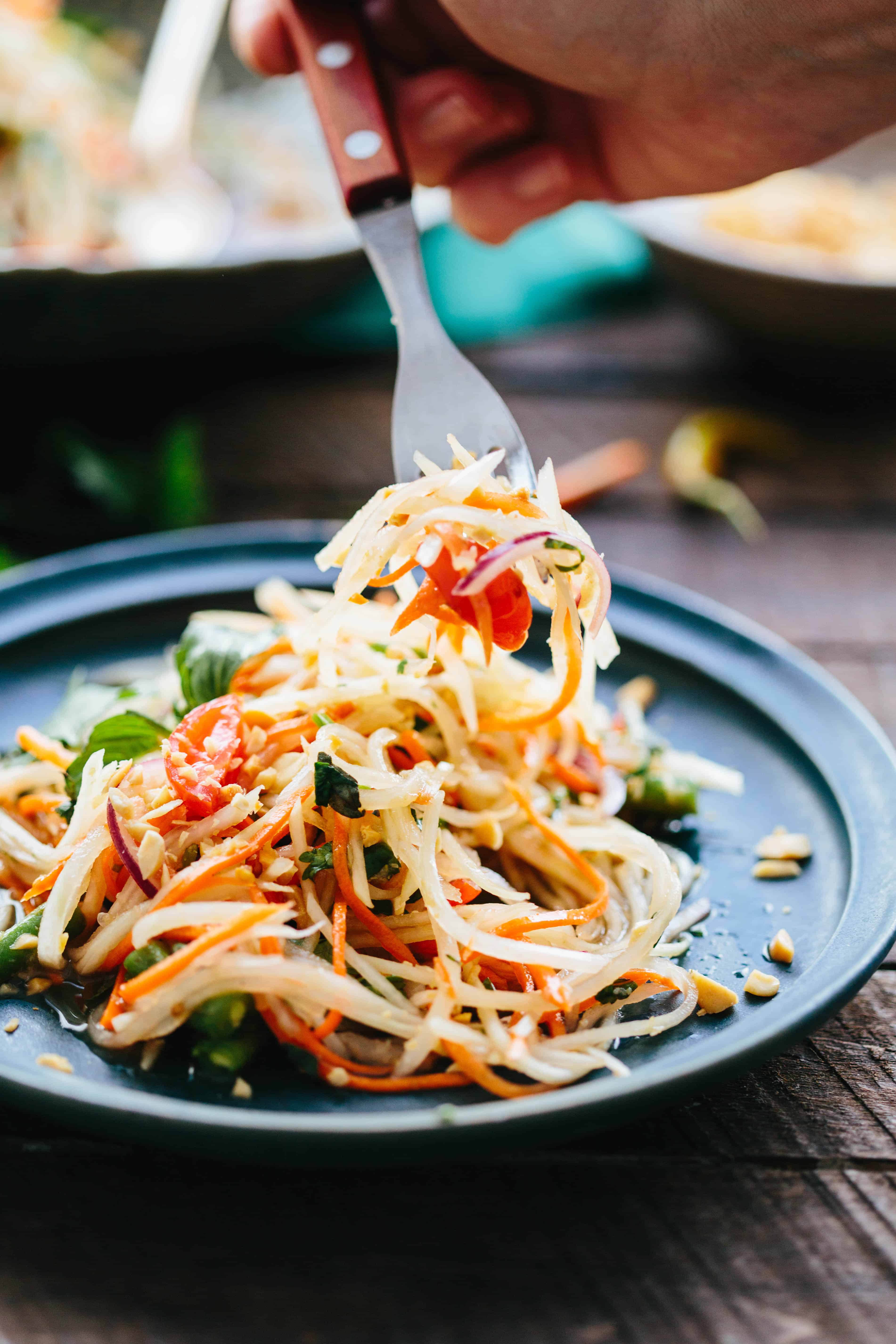 A fork pulling off a bite of shredded Thai green papaya salad from a plate.
