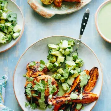 Dinner plate loaded with chicken thighs, diced avocado salad, and sweet potato wedges.