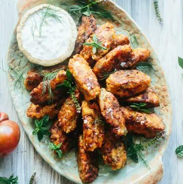 Fried Greek tomato fritters stacked on an oval platter with a bowl of tzatziki.