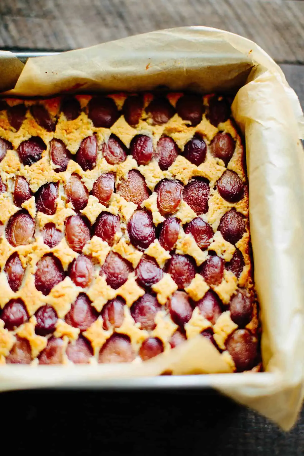 Parchment lined baking sheet with peanut butter shortbread bars with grapes just pulled out of the oven.