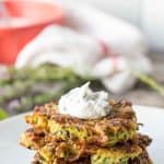 A stack of zucchini fritters topped with sour cream.