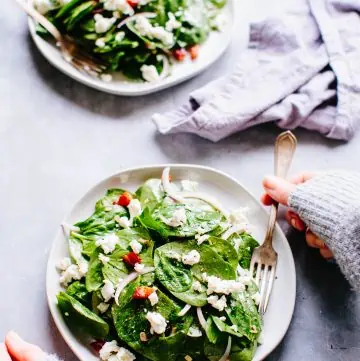 A plate of spinach salad with a fork and a hand