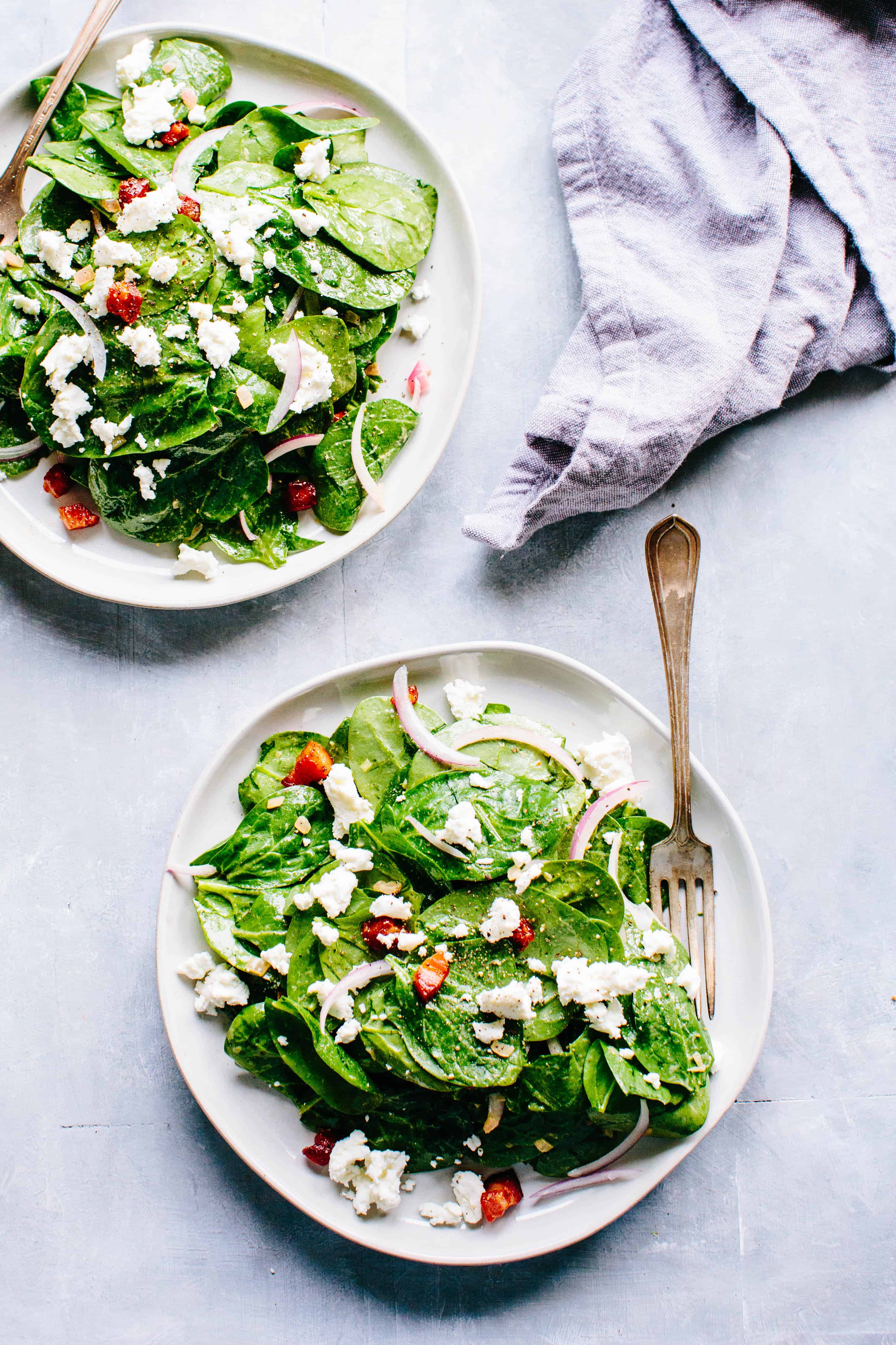 A table with 2 plates of spinach salad, one with a fork