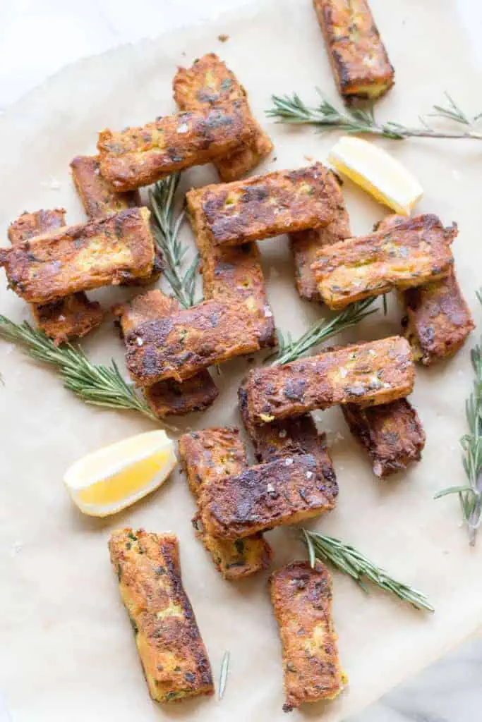 A stack of chickpea veggie fritters with rosemary sprigs and lemon wedges.