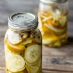 Two half gallon mason jars of dill pickle slices on a wood table.