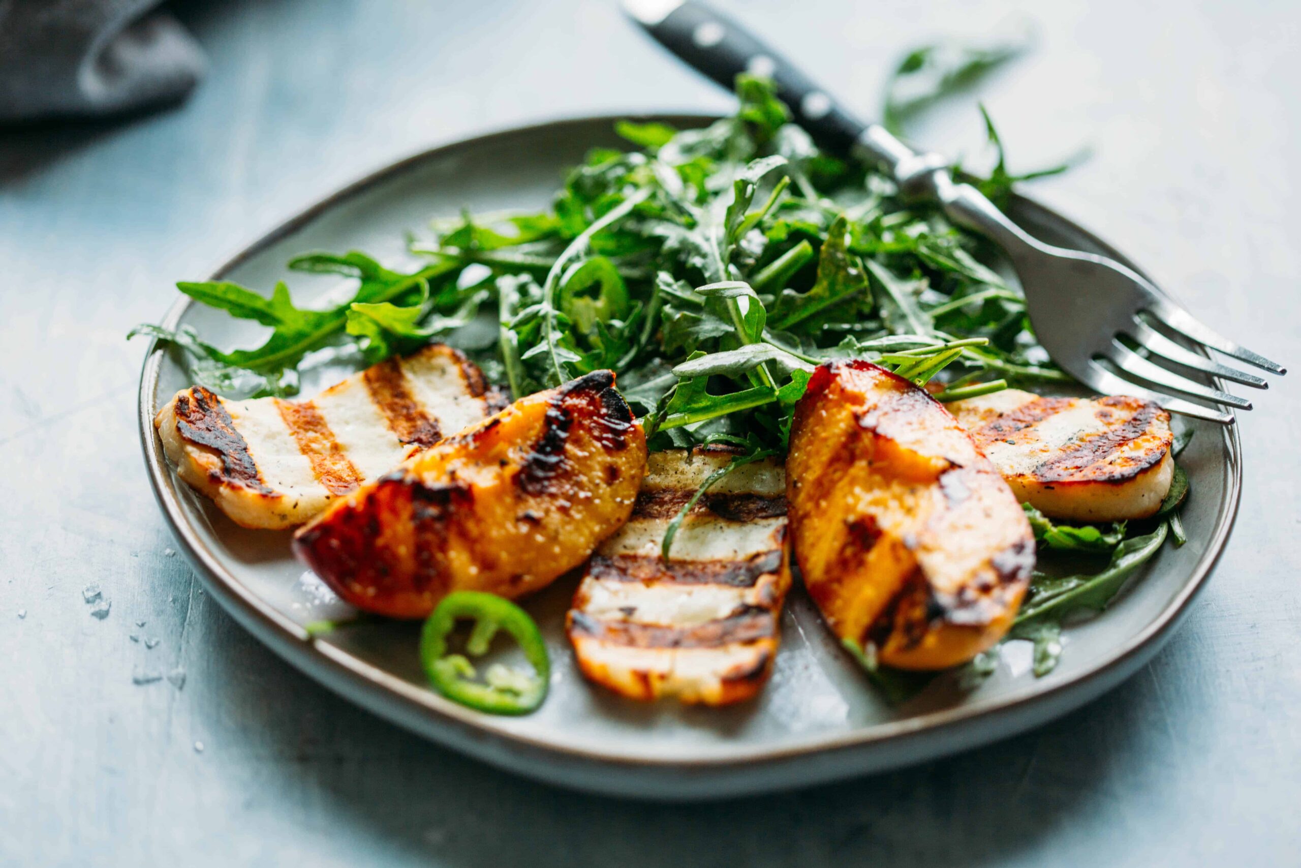 close up of grilled halloumi and peaches with arugula, jalapeños and honey lemon vinaigrette with a fork