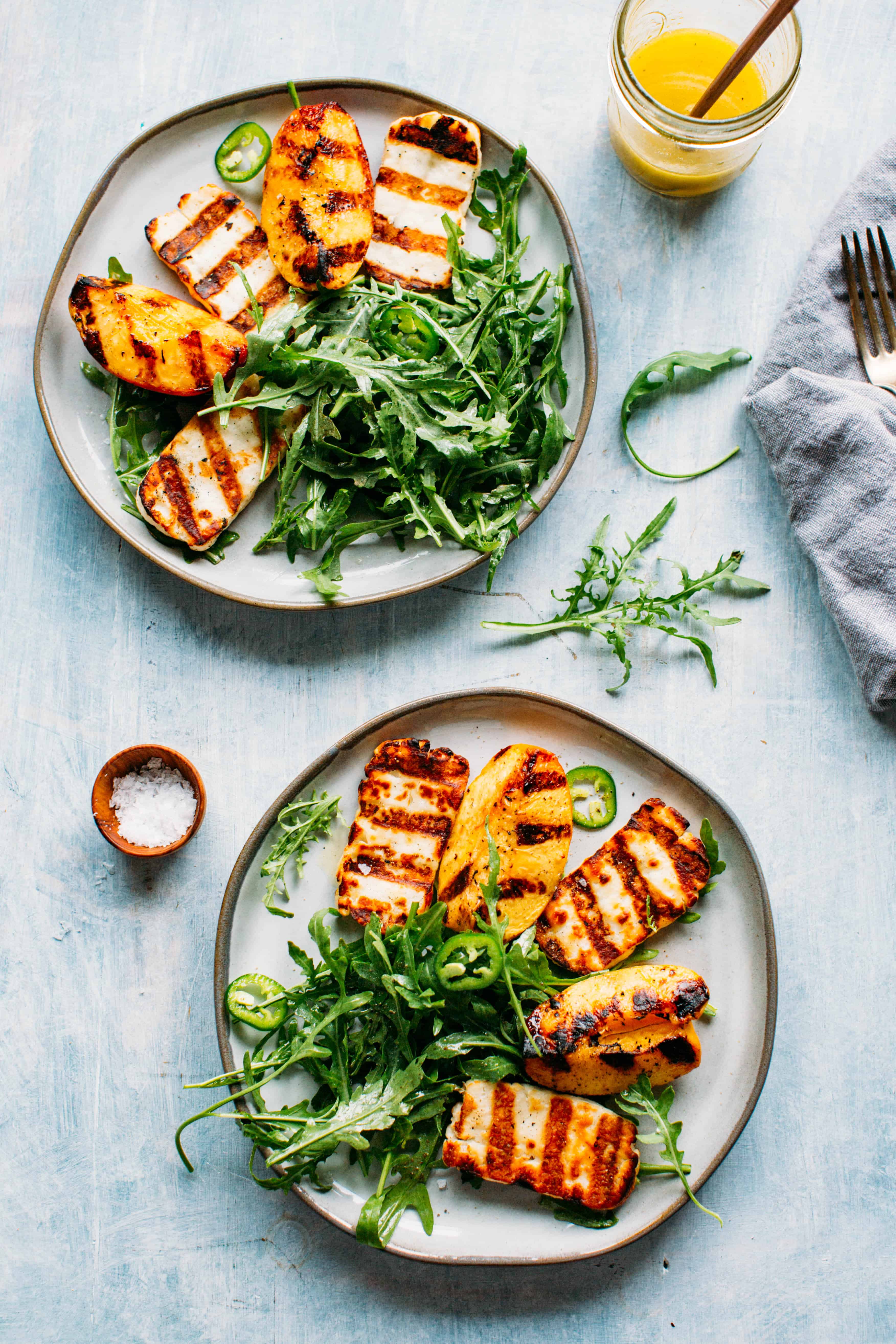 Two plates of grilled halloumi and peaches with arugula, jalapeños and honey lemon vinaigrette