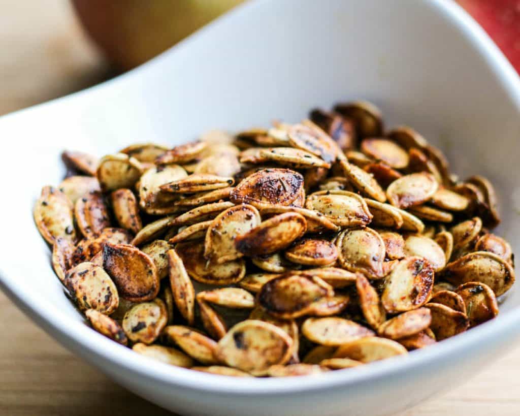 Close up of a small white bowl of brined and roasted pumpkin seeds.