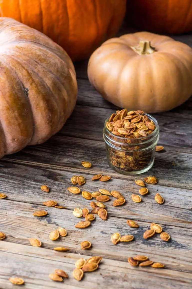 Roasted pumpkin seeds in a small mason jar on a wood surface with loose seeds sprinkled around.