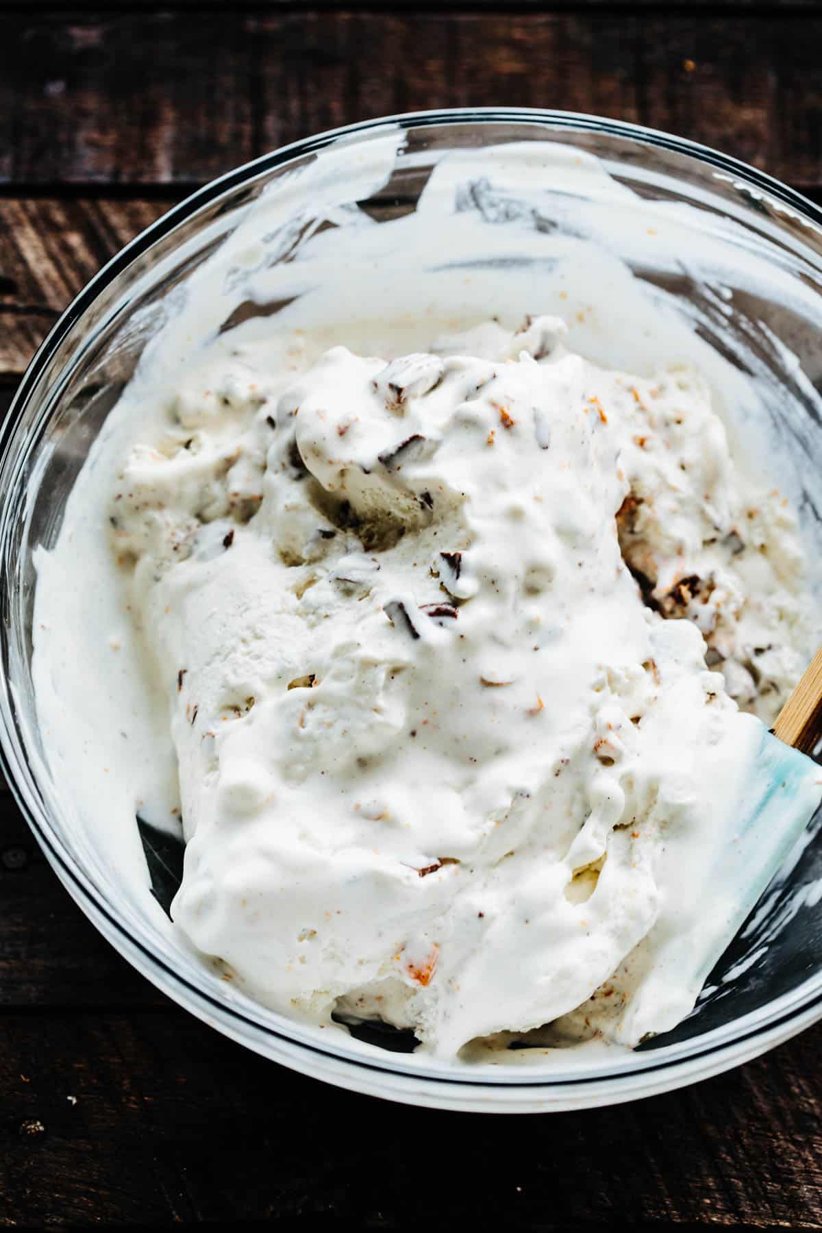 bowl of vanilla ice cream with chopped candy mixed in and a rubber spatula