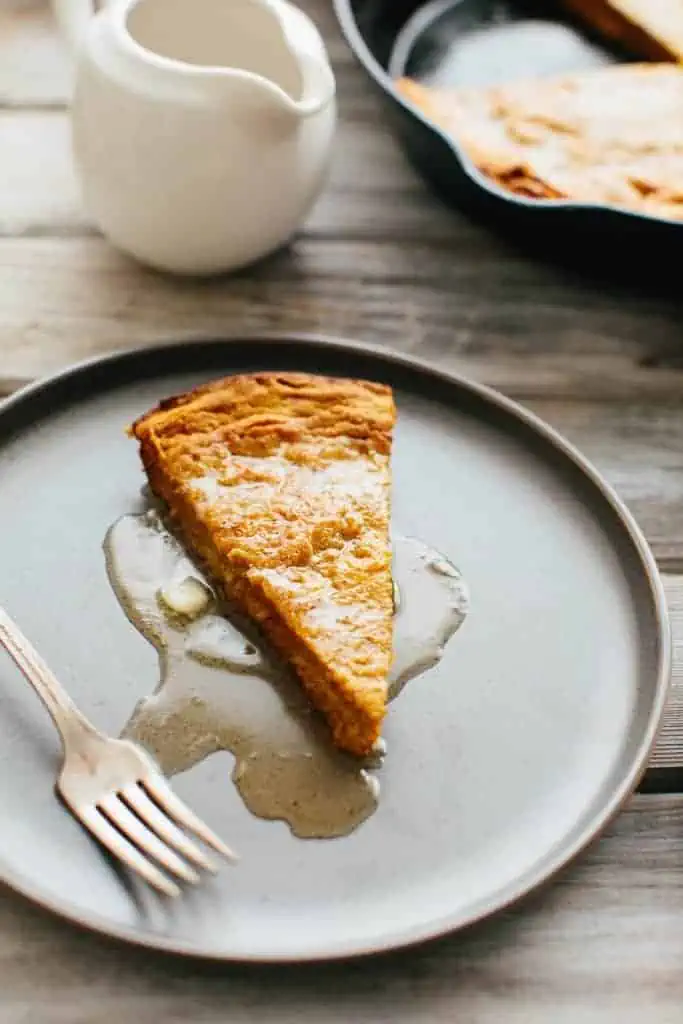 A plate with a slice of Dutch baby with maple syrup and a fork