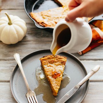 maple syrup being poured on a slice of Oatmeal Pumpkin Dutch Baby