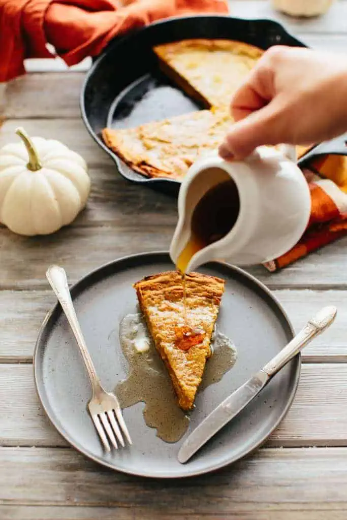 maple syrup being poured on a slice of Oatmeal Pumpkin Dutch Baby