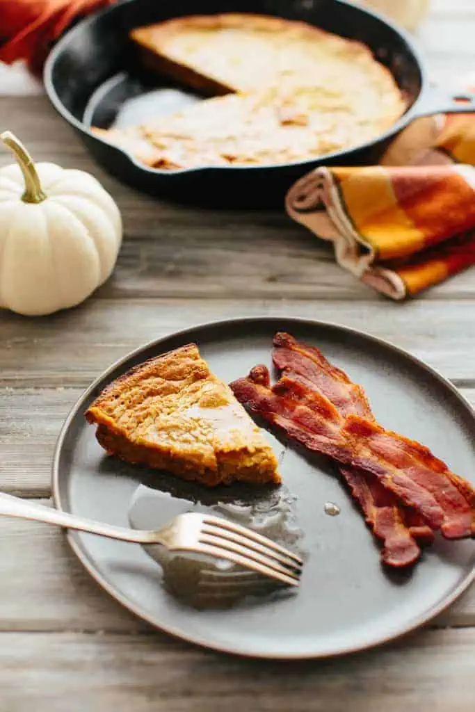 Slice of oatmeal pumpkin Dutch baby with bacon on a dark plate.