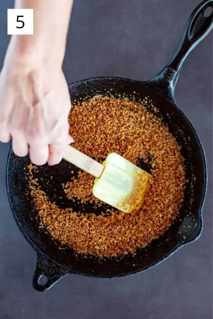 stirring toasted panko in a cast iron skillet with rubber spatula