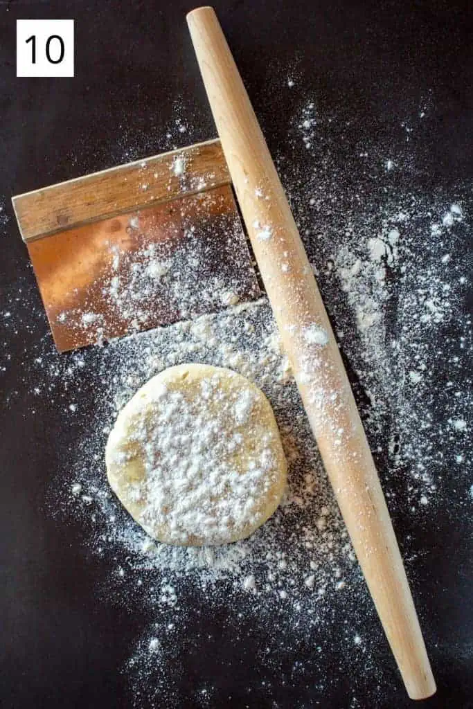 disc of pie dough, rolling pin and bench scraper dusted with flour on dark background