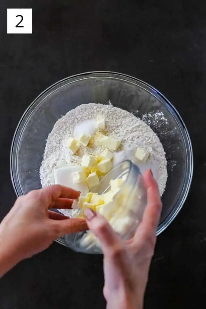 two hands adding butter and shortening to a bowl of dry ingredients