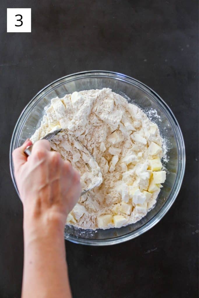 hand using a pastry cutter to cut butter and shortening into a bowl of flour