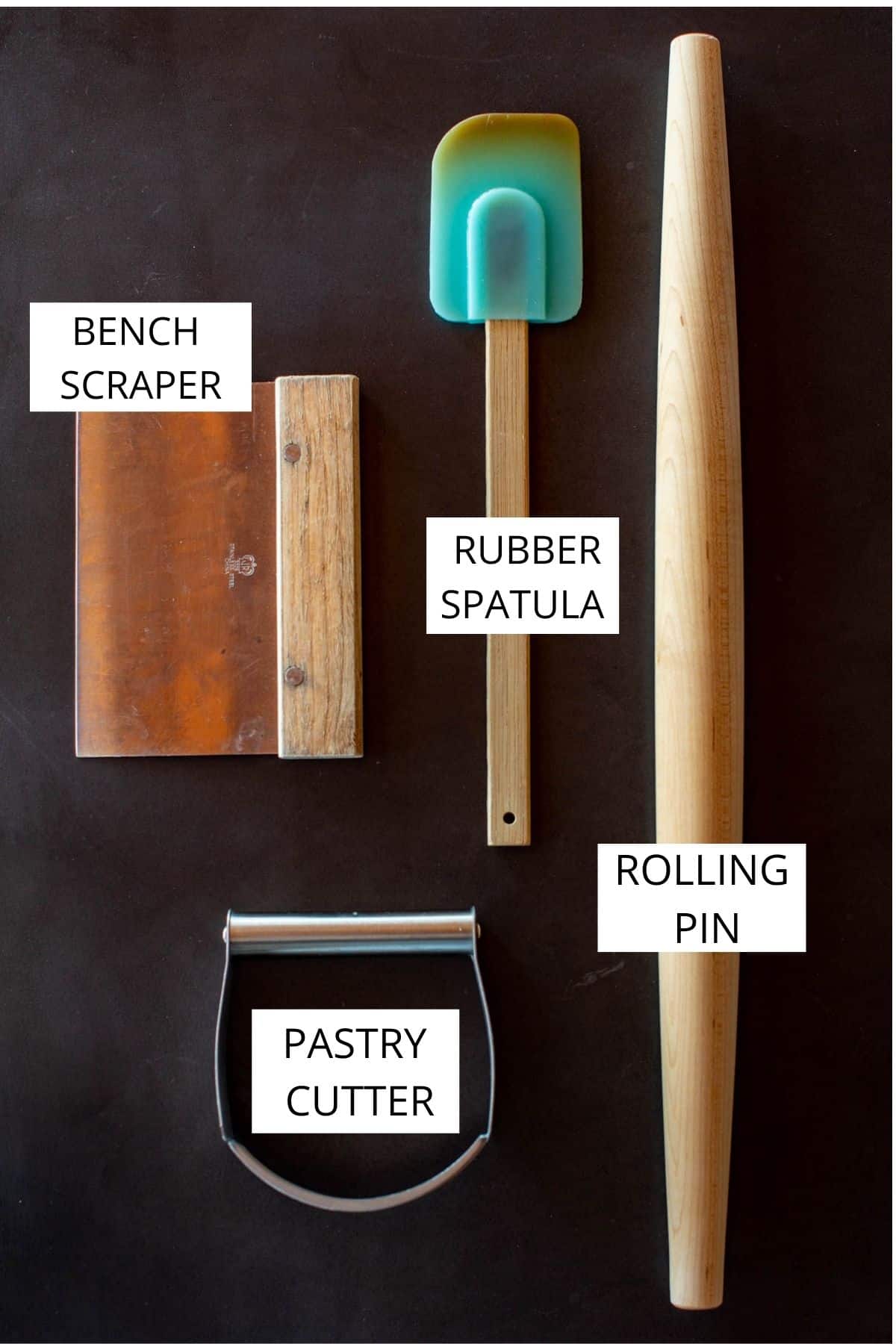 Labeled overhead shot of tools needed for flaky pie dough on dark background.